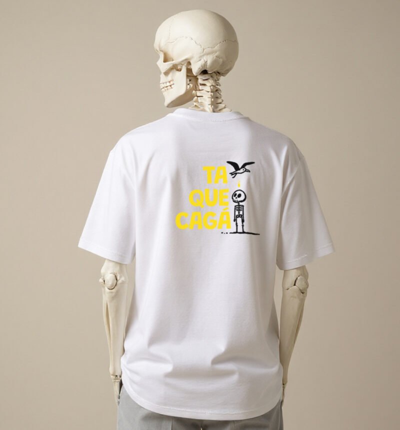 La imagen muestra a un esqueleto luciendo la parte trasera del diseño Cagao, de la línea de polos clásicos perteneciente a la Colección Calacas, en versión blanca.